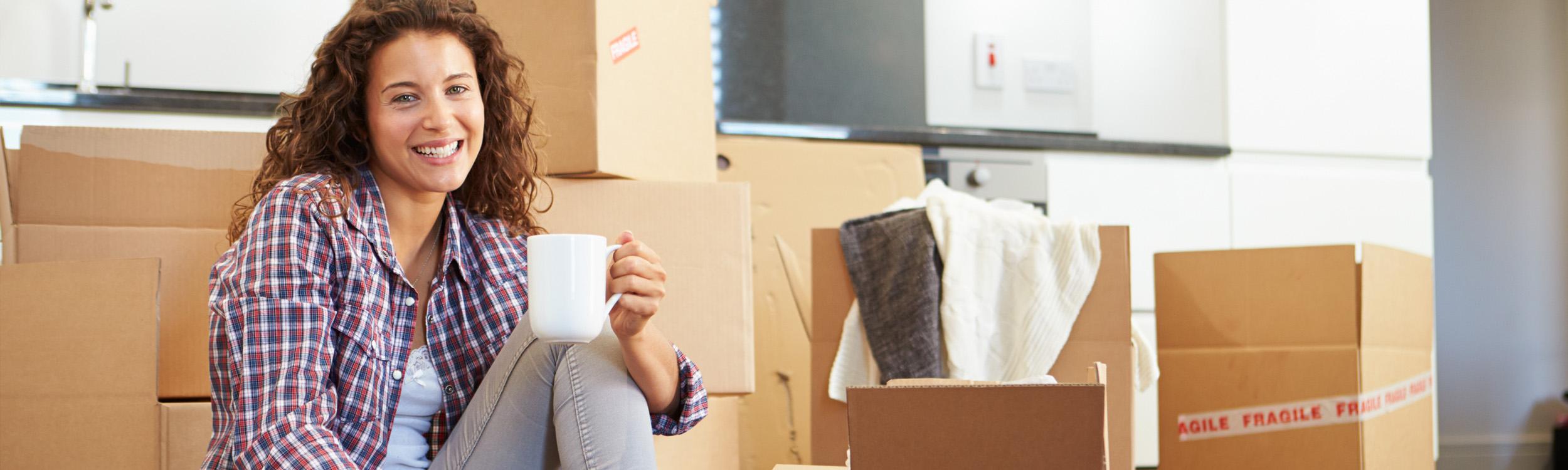 girl holding coffee sitting on the floor with moving boxes